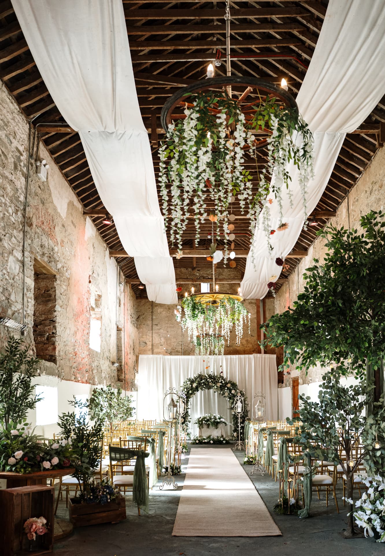 Long view down the barn aisle beneath the timber roof and floral chandelier