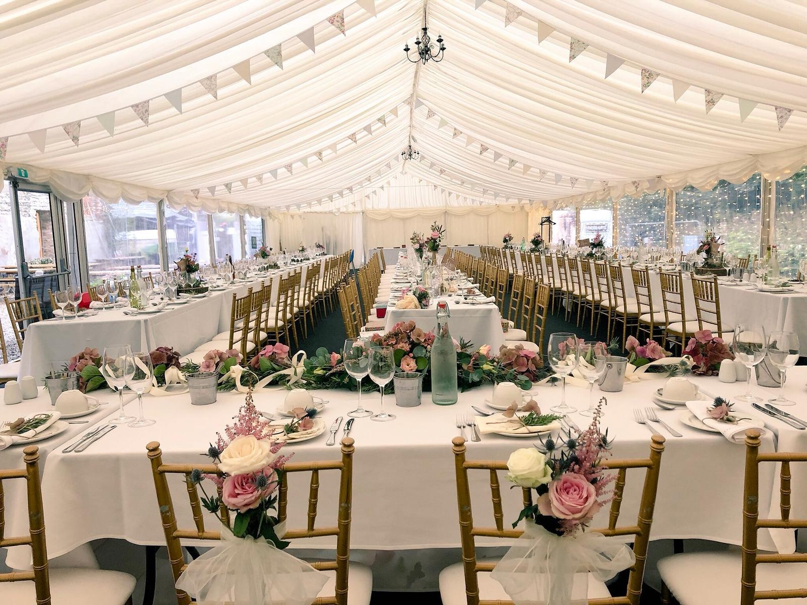 Marquee laid for a wedding breakfast with bunting, gold chairs and pink floral runners